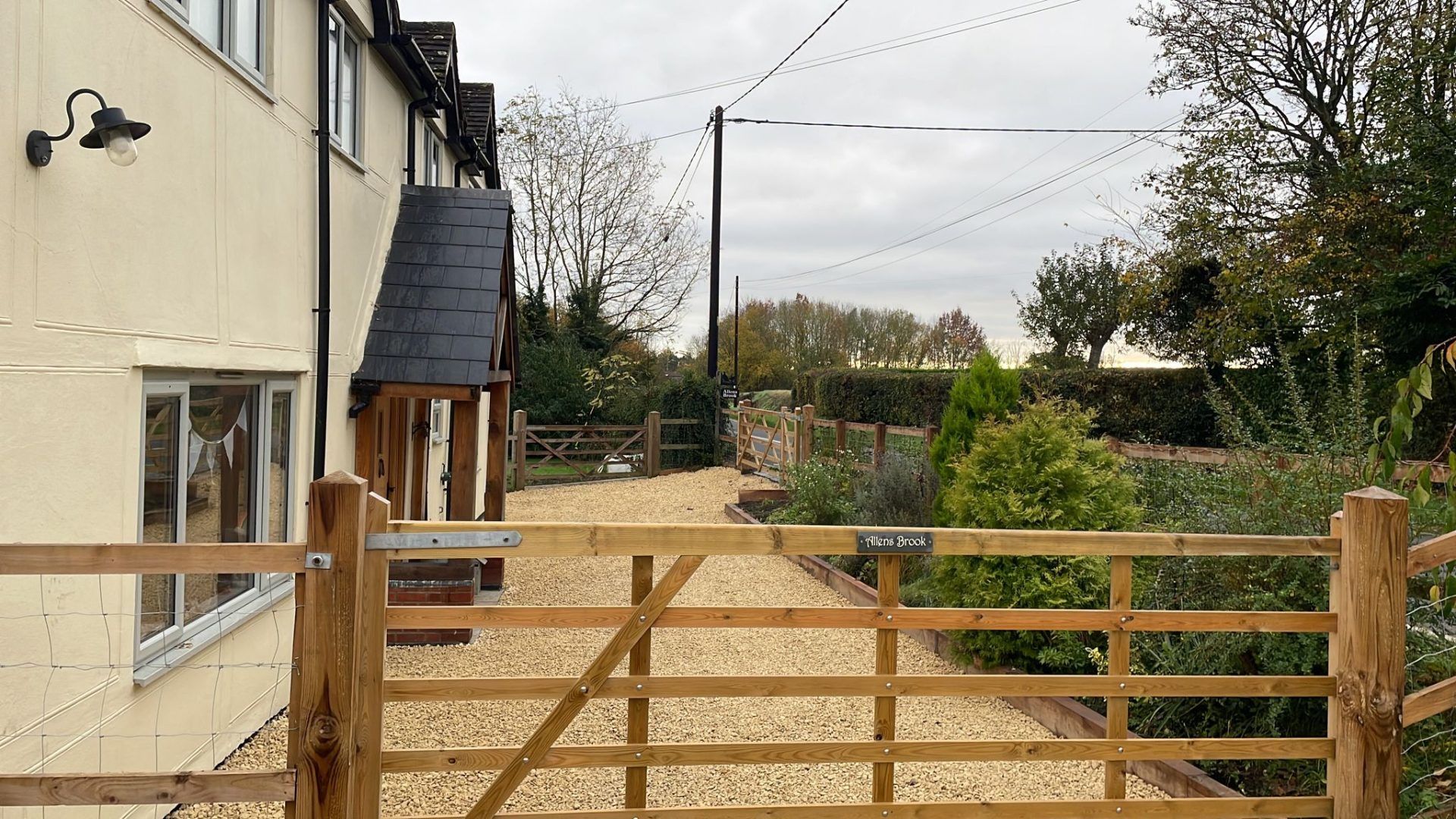 Side view of cream coloured house looking through new wooden gate to newly laid shingle driveway.