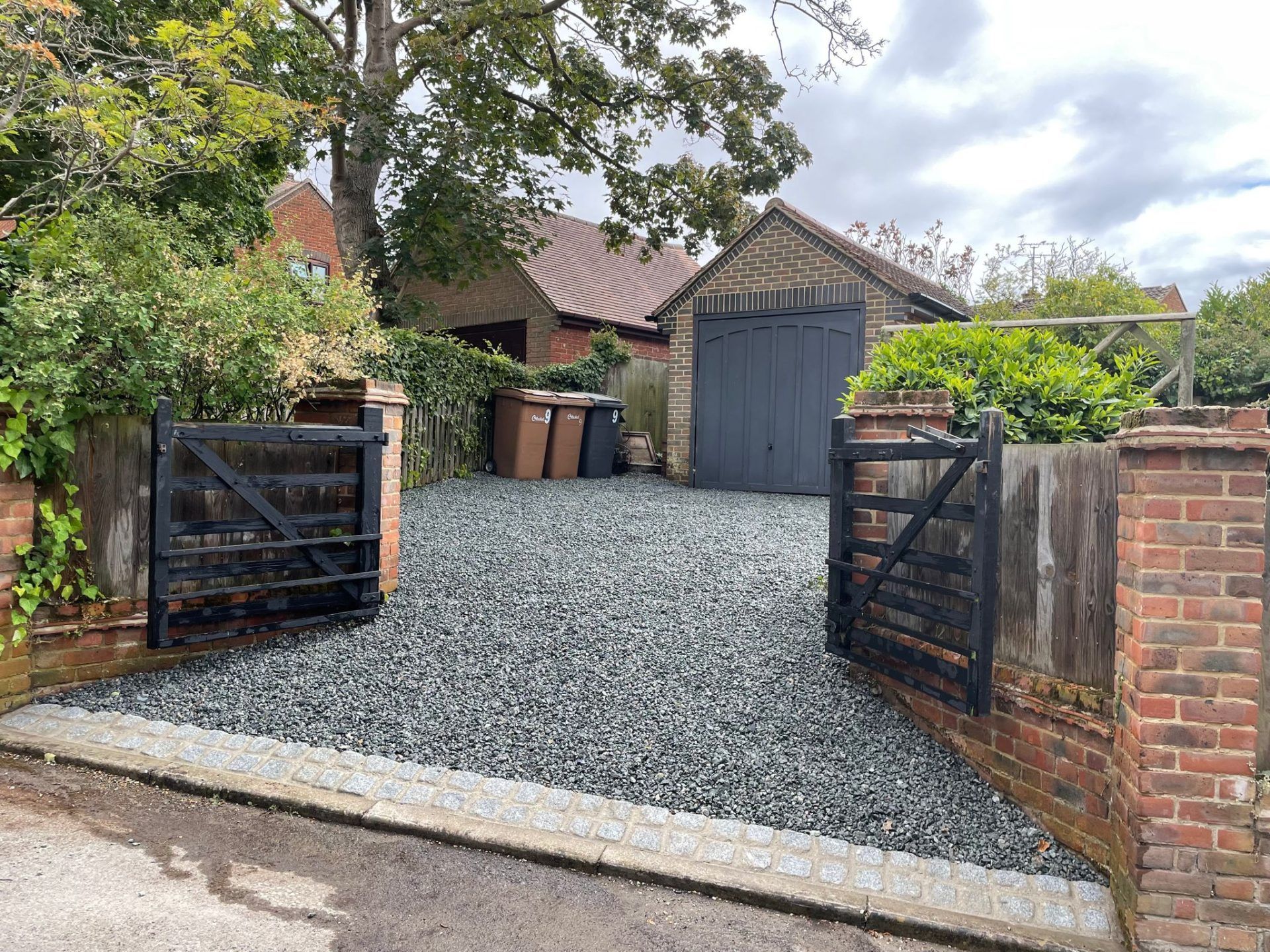 Two black gates open to driveway laid with grey chippings.