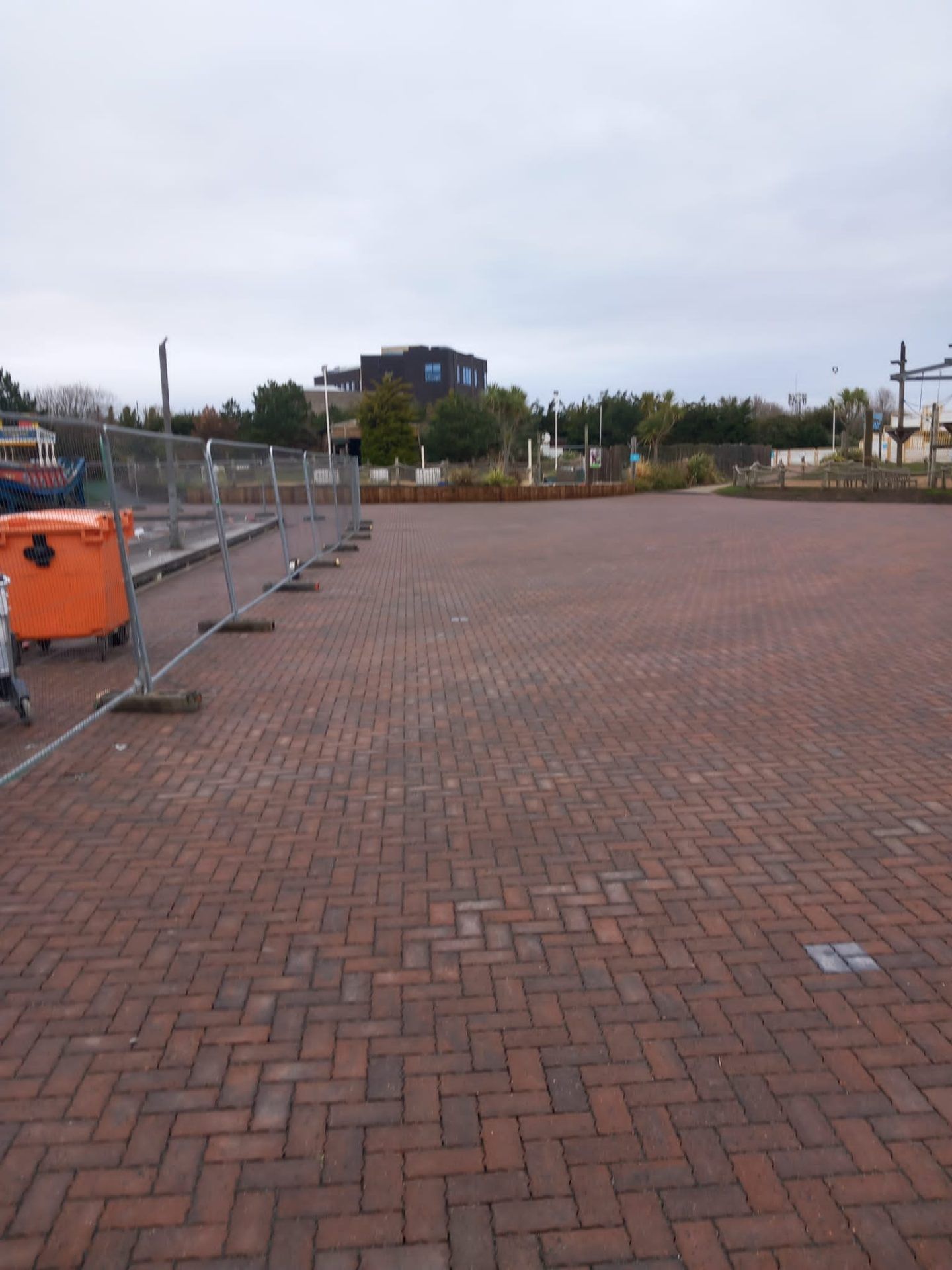 Expanse of new block paving with temporary fence alongside and buildings behind.