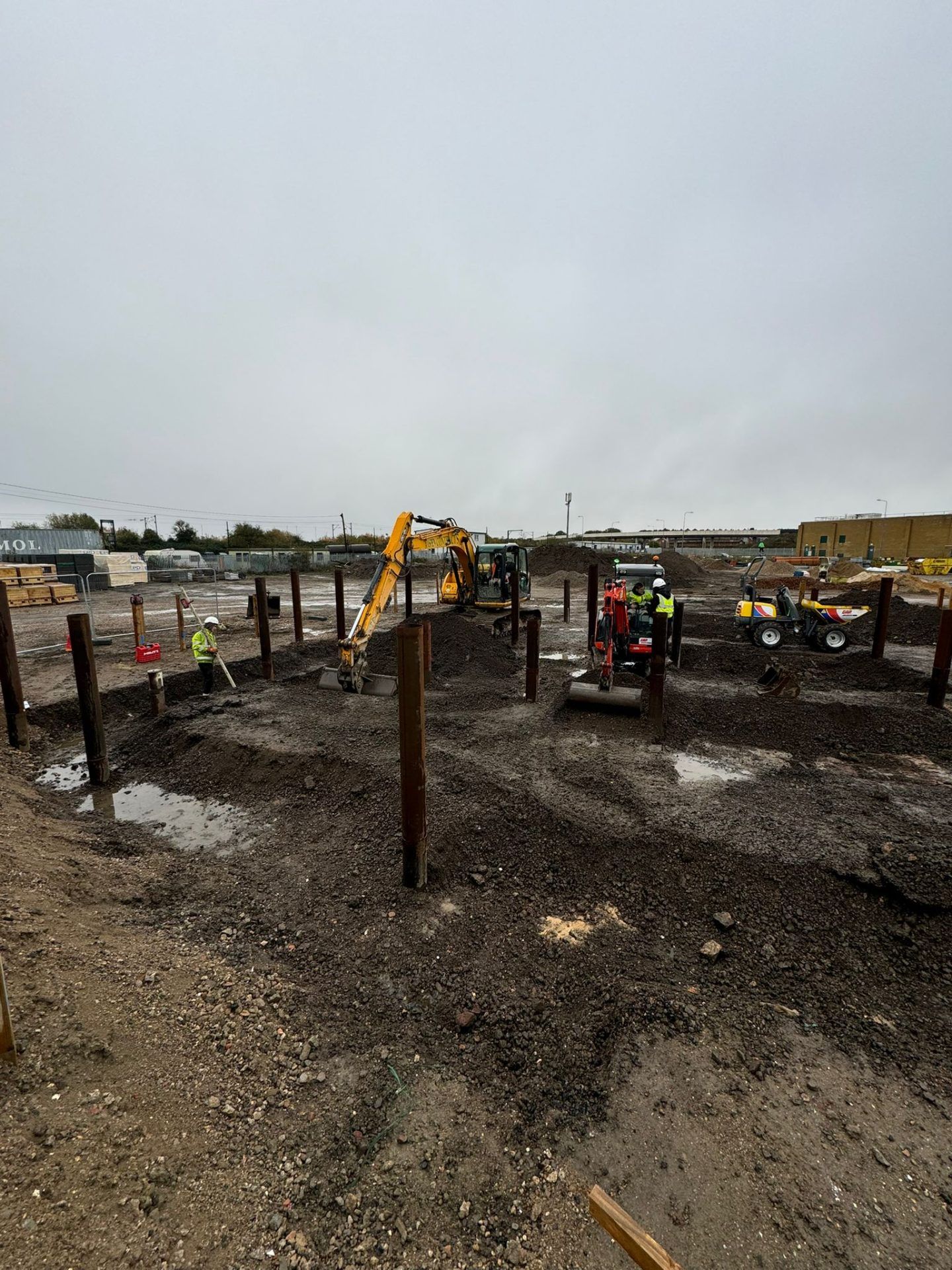 Groundworks with yellow mechanical digger and several workmen in high vis yellow jackets and white hard hats.