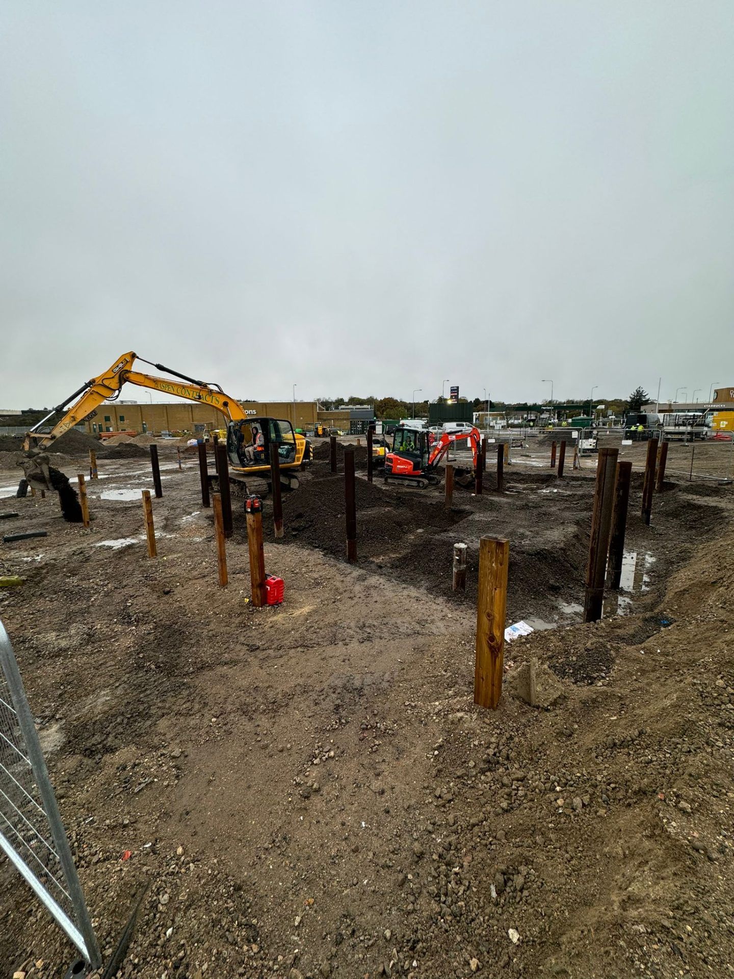 Yellow mechanical digger moving soil with red mini digger in background.