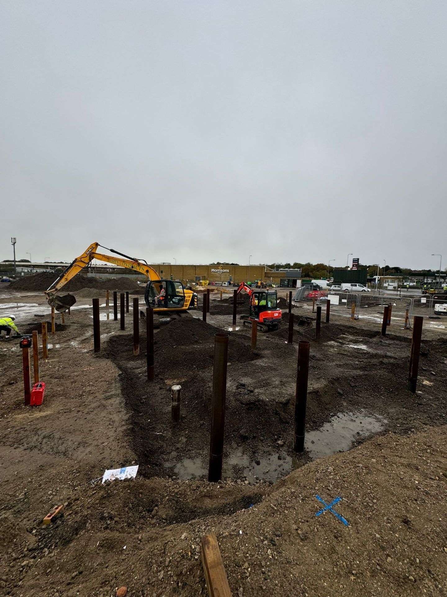 Yellow mechanical digger moving soil with red mini digger in background.