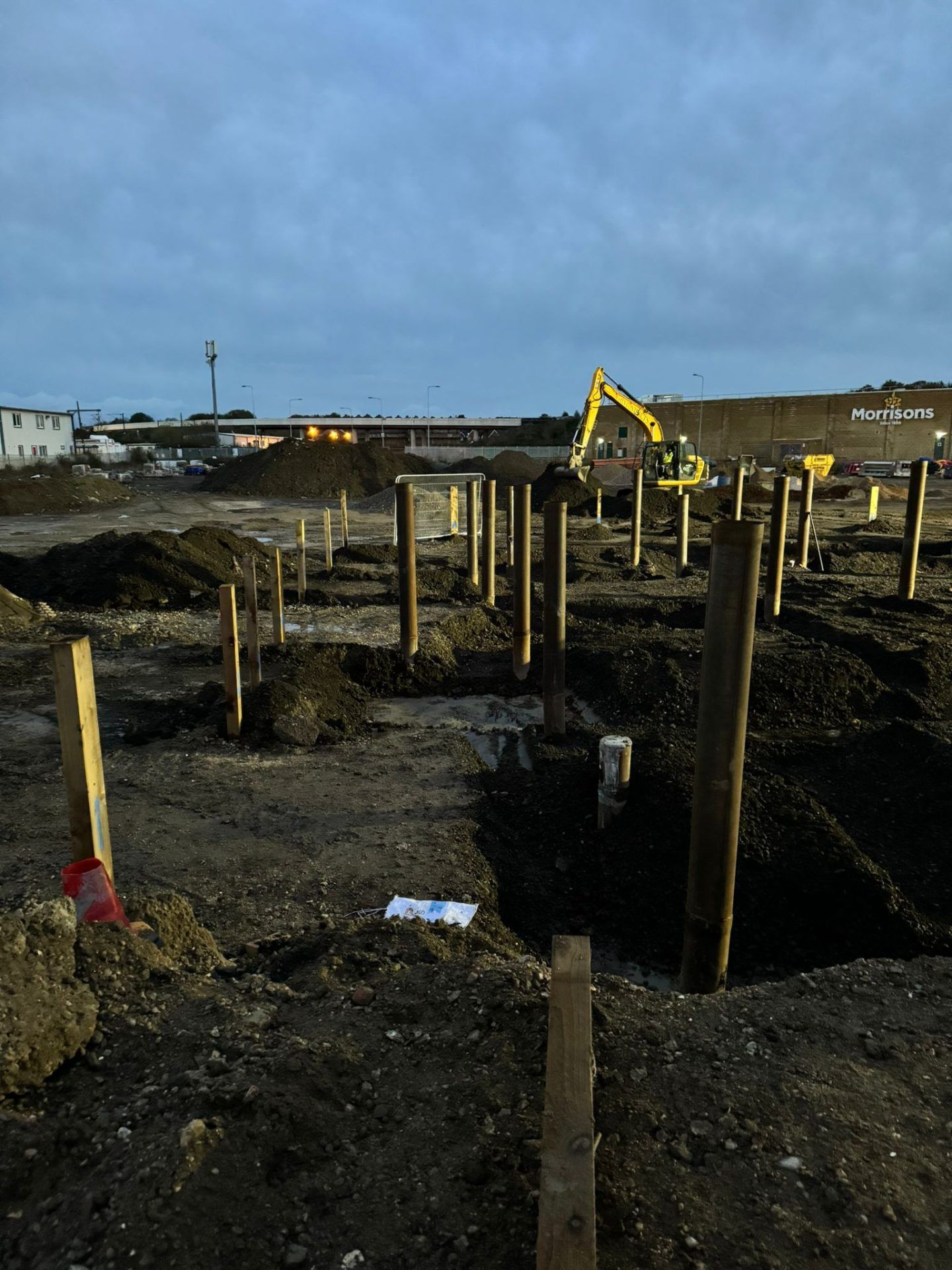 Excavated building site with yellow mechanical digger in background.